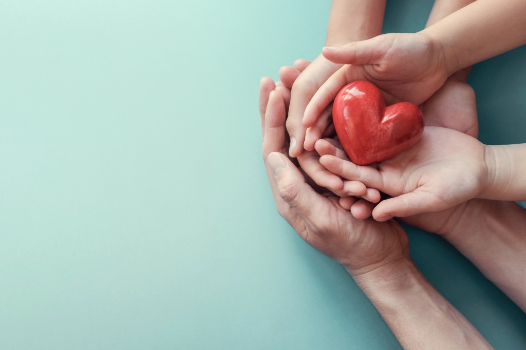 adult and child hands holding red heart on aqua background, hear