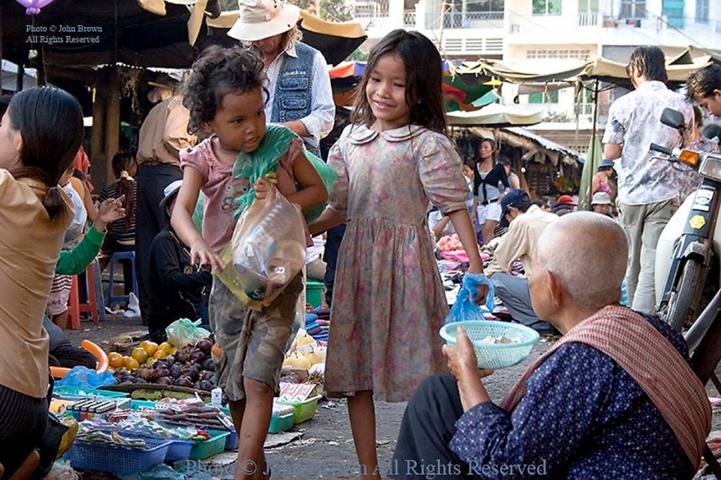 Two young street children girls are walking past an elderly woman begging for money in Phnom Penh, Cambodia.